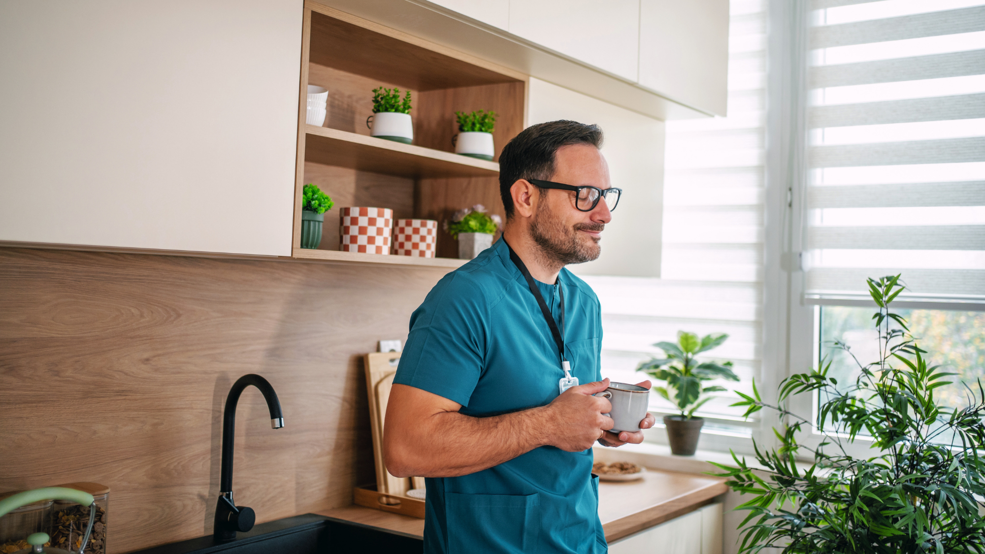 Male nurse drinking from a mug in a kitchen.