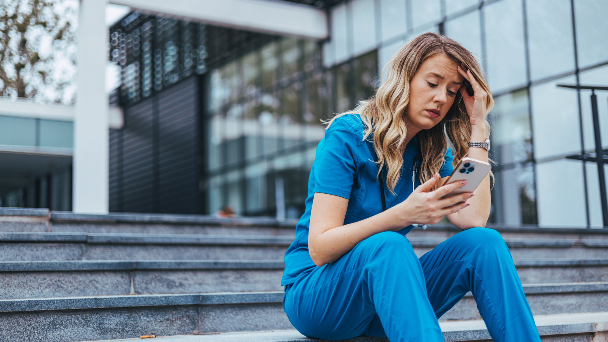 Female nurse burnt out looking at her phone while sitting on stairs.