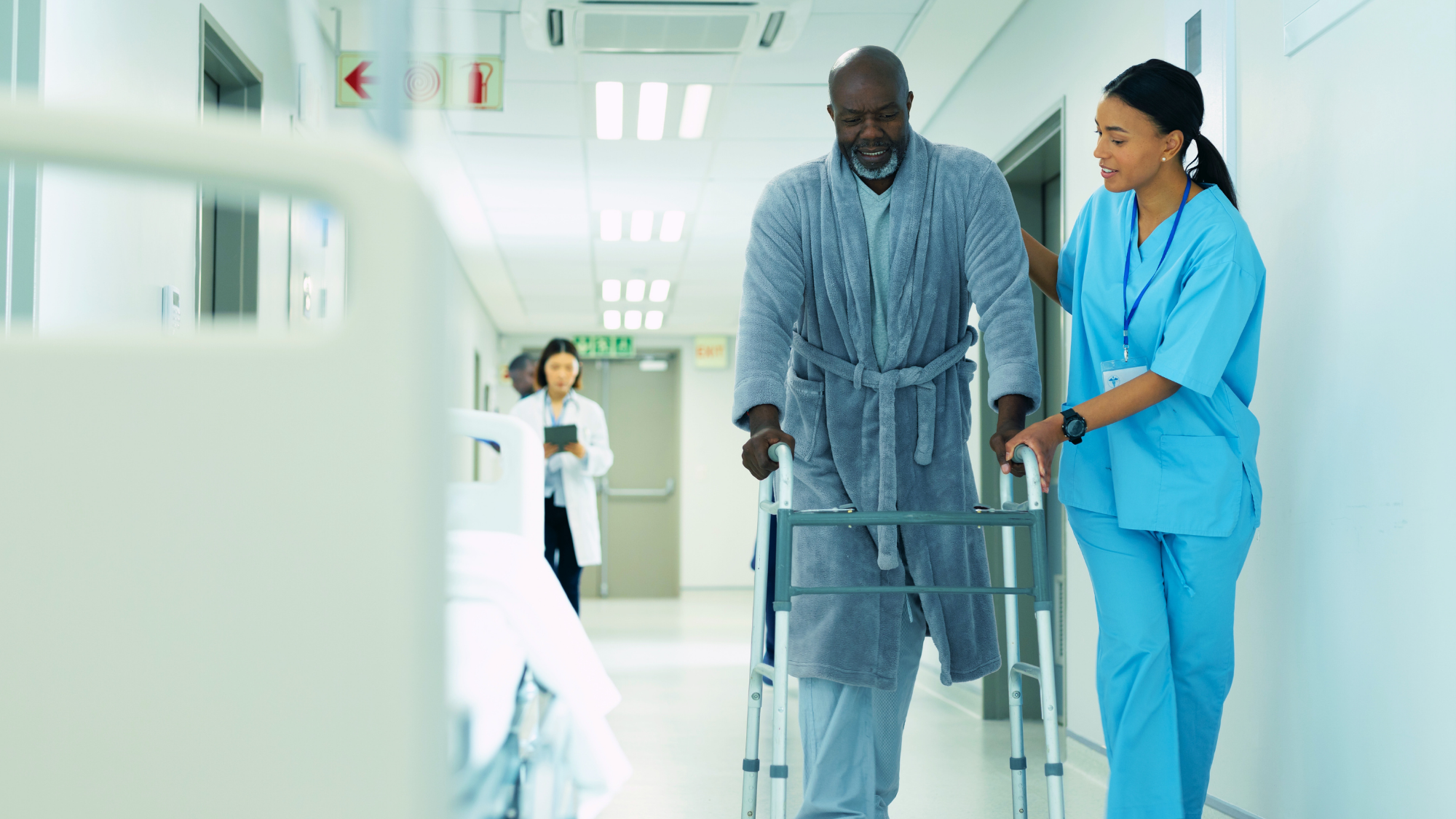 Female nurse helping an older patient in the hallway with a walker