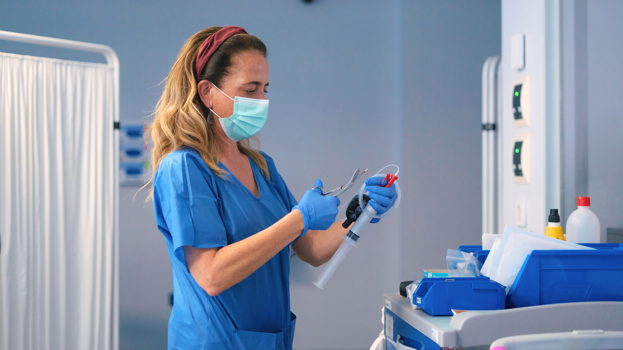 Female nurse in blue scrubs wearing a mask using scissors