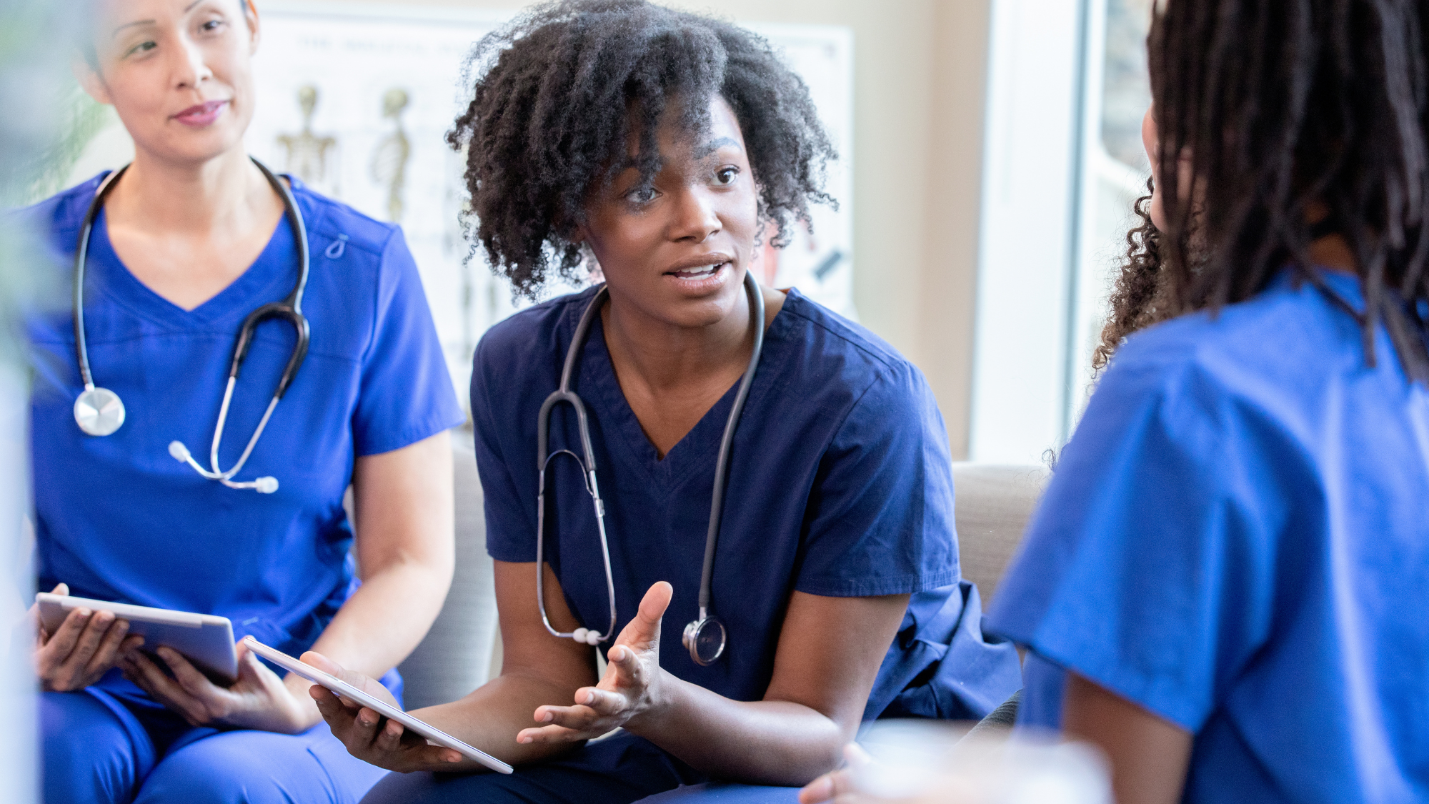 Three clinicians in blue scrubs sitting and discussing healthcare workforce solutions