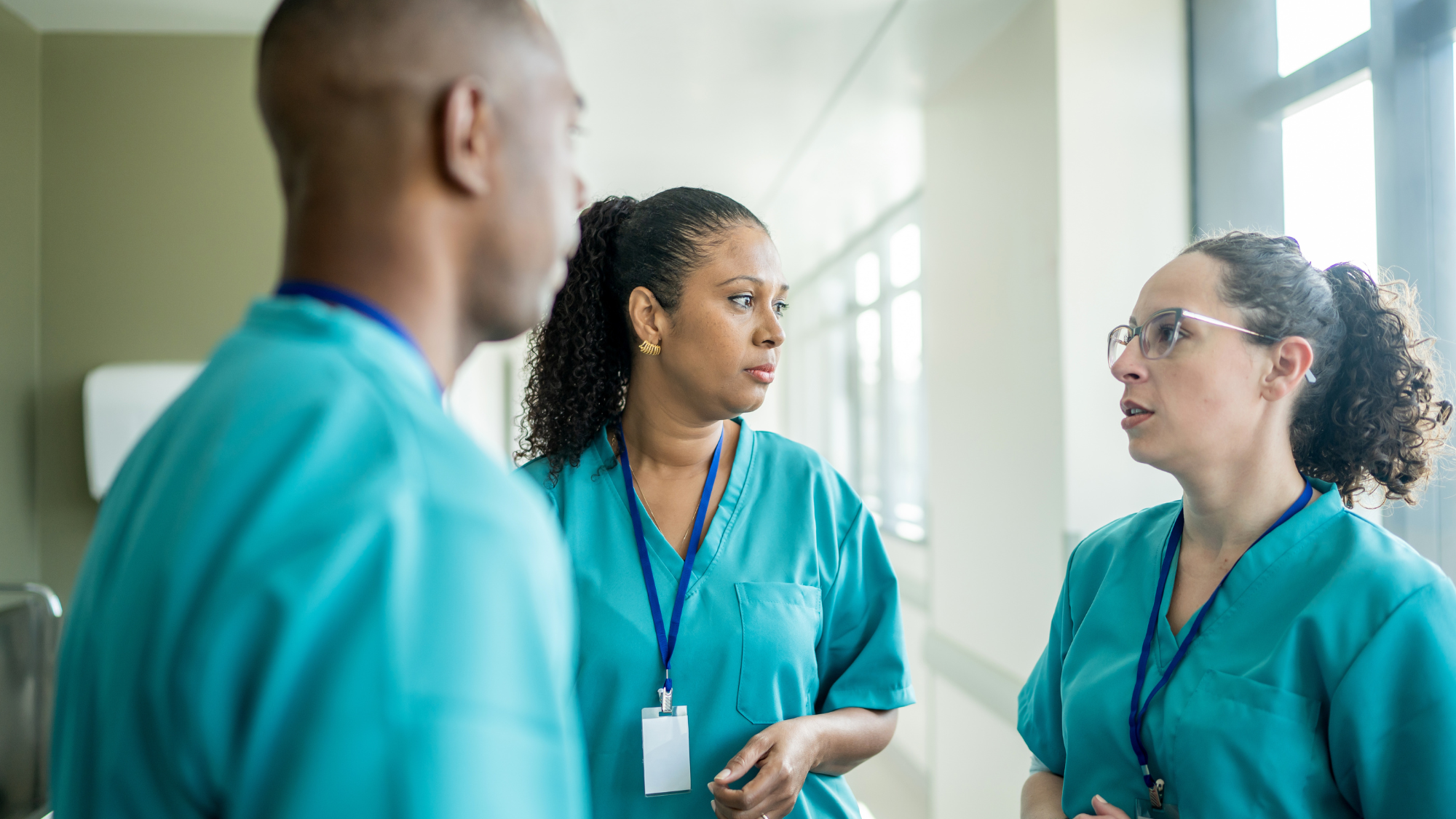 Three clinicians in teal scrubs discussing healthcare workforce solutions planning in semicircle