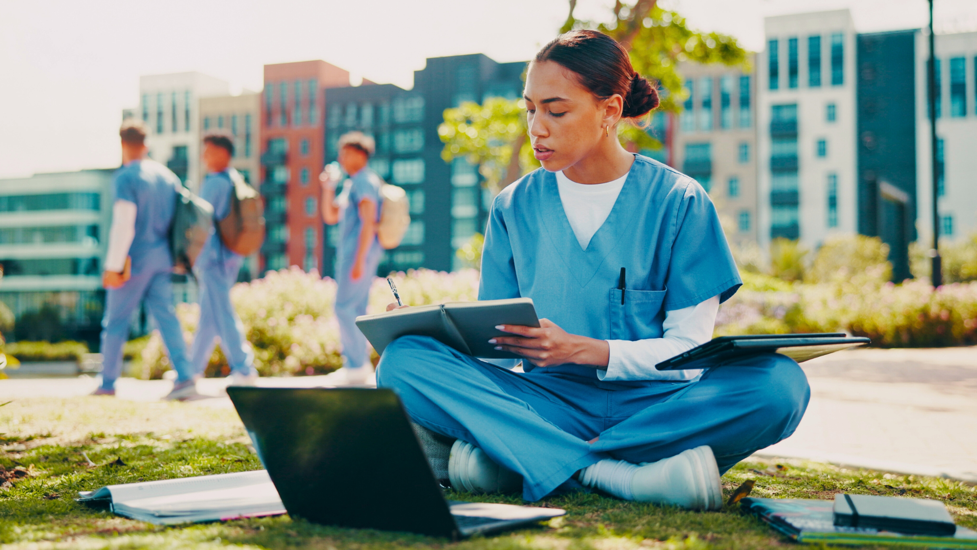 Female nurse sitting in a park studying with her computer and notebook.