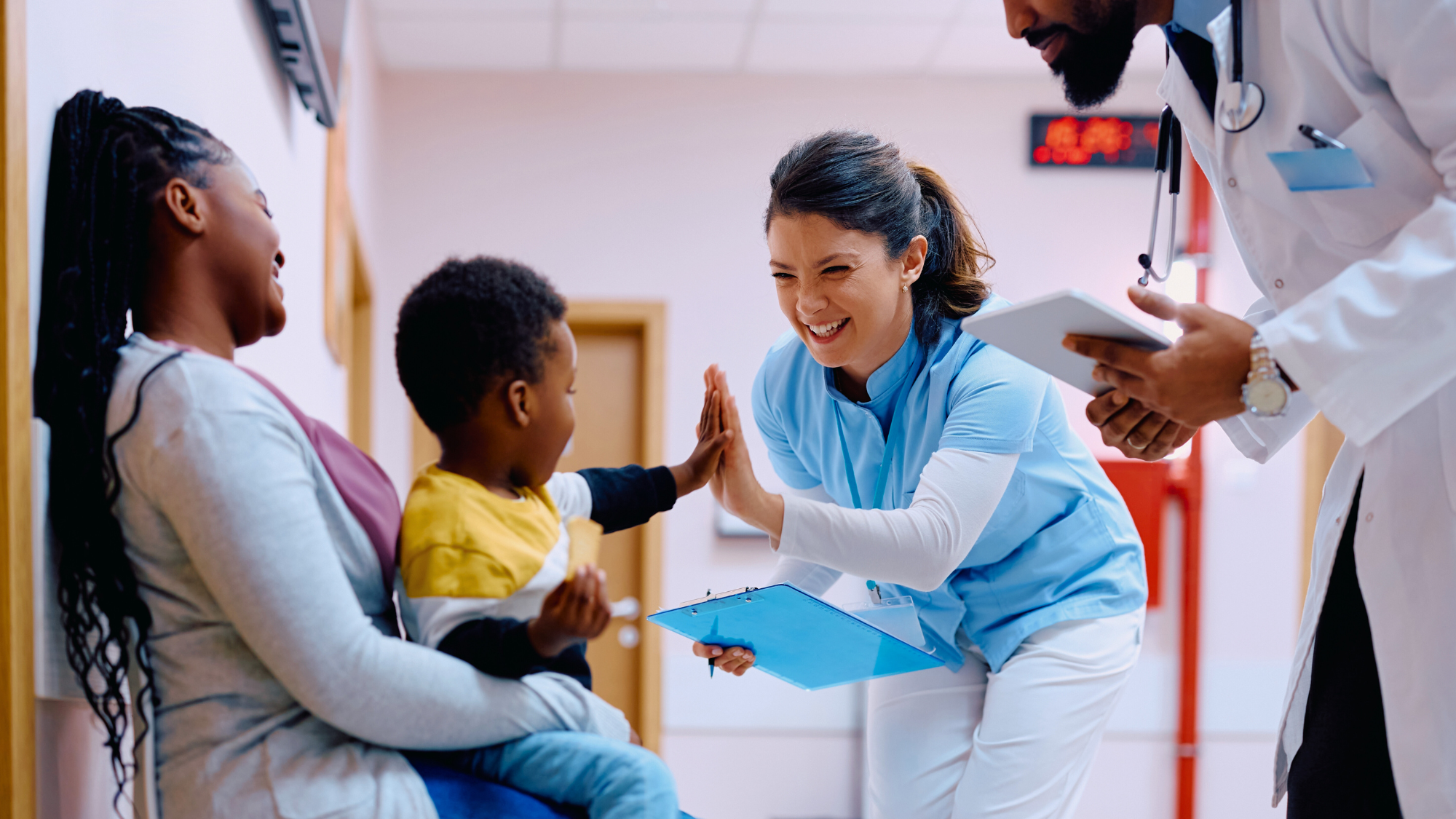 Female nurse high-fiving little boy sitting on his mom's lap.