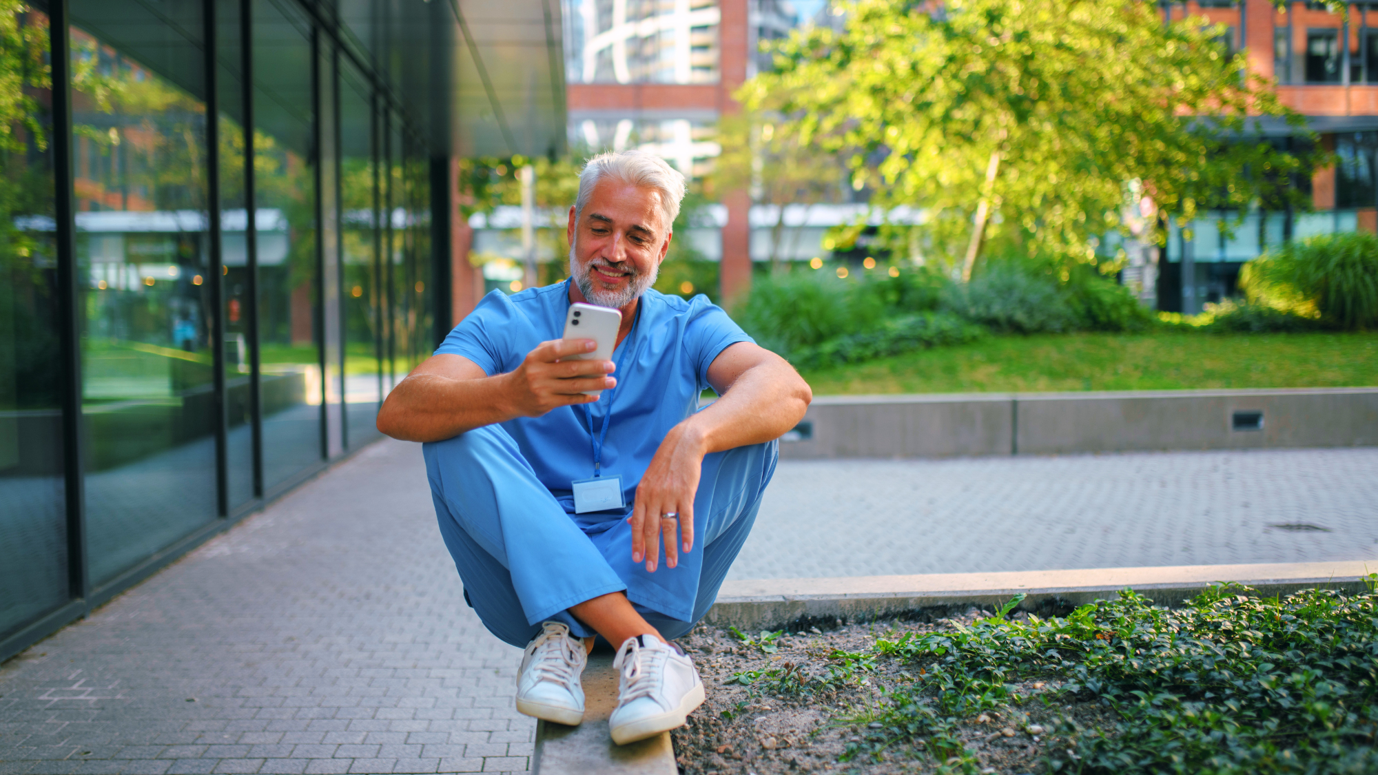 Older male nurse sitting down looking at his phone.