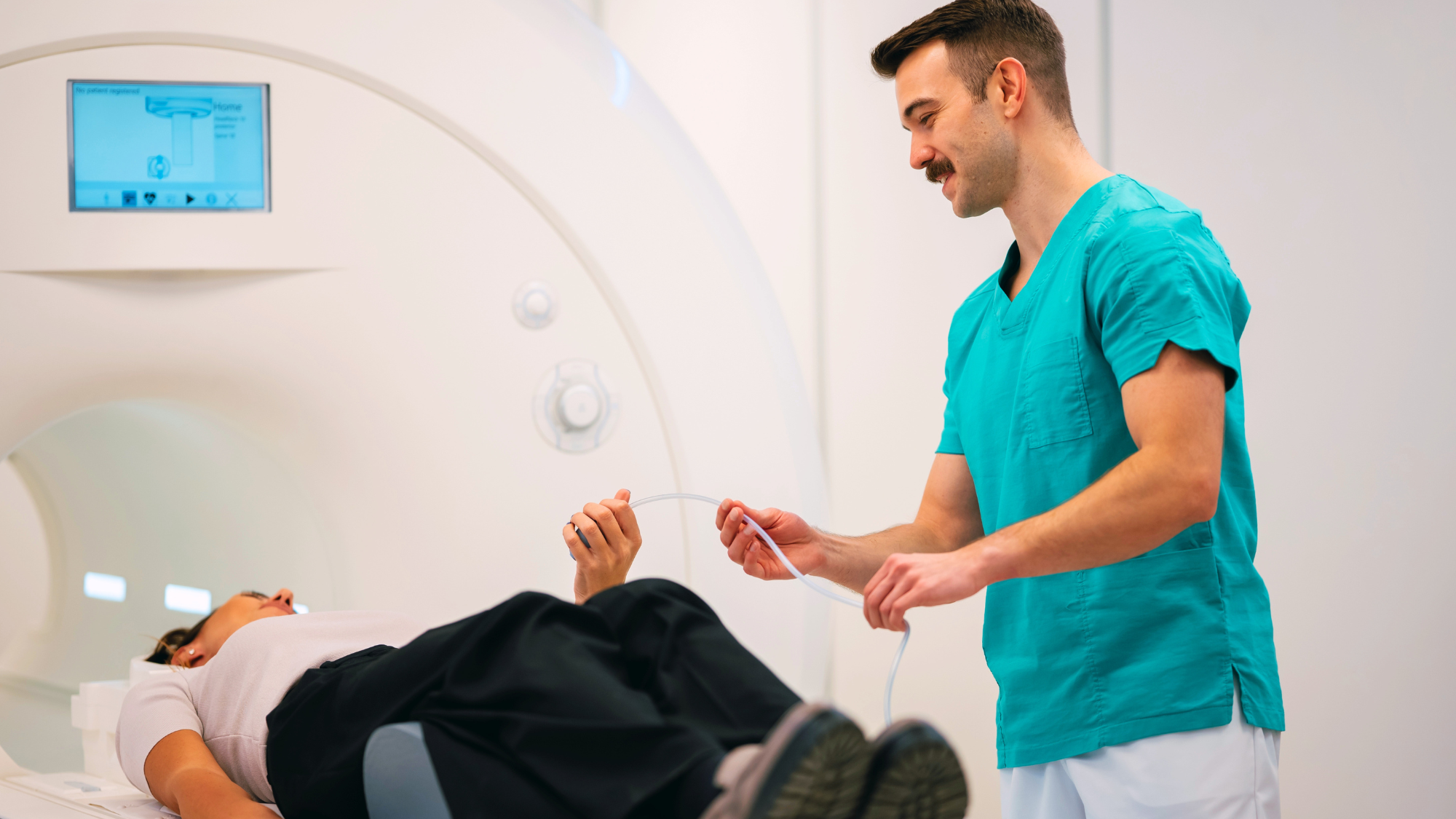 Male MRI tech helping another male into an MRI machine.